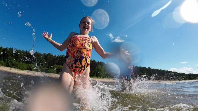 Two little girls running on water on a summer sea beach and having fun. Slow motion.