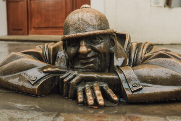 A bronze statue of a man peeking out from the pavement in Bratislava showcasing local art and...