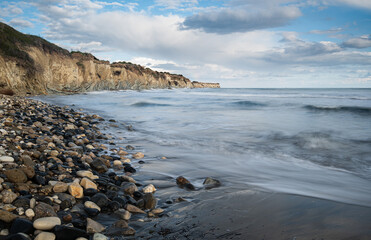 Sea waves crashing on rocky beach with cliffs in background. Cyprus seascape