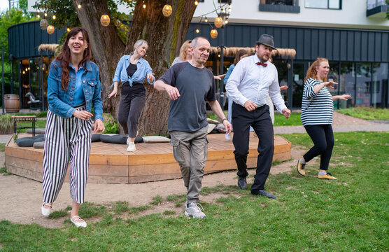 Cheerful dance party outdoors, featuring individuals of different ages enjoying the festive ambiance under illuminated string lights. They are dancing swing dance in summer city park