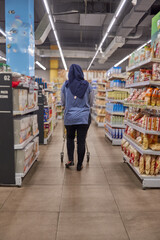 Asian woman wearing hijab shopping at supermarket looking for daily needs between store shelves
