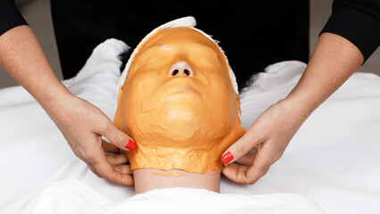 Close-up of a cosmetologist removing an alginate mask in a contemporary skincare center. This scene...