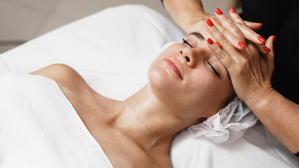 Close-up of a masseur's hands performing a relaxing facial massage on a young woman in a beauty salon. This scene highlights professional care and the soothing benefits of a spa treatment.