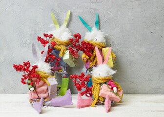 Christmas character family of rabbits with colorful ears in a sweater with gifts in their hands on the background of a gray wall