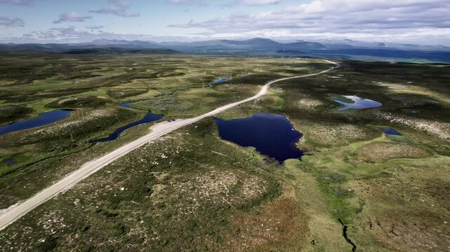 Flying backwards over the Flatruetv&auml;gen dirt road, surrounded by ponds and tundra of Flatruet landscape, with the V&aring;l&aring;dalen Nature Reserve mountains in view. Wilderness of J&auml;mtland, H&auml;rjedalen, Sweden