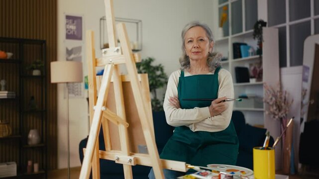 Portrait of senior woman artist painting a picture at easel stand, art therapy