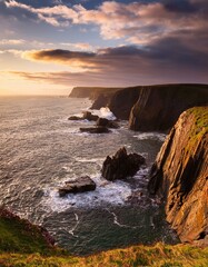 Obraz premium Dramatic coastal cliffs and rock formations under a cloudy sunset sky