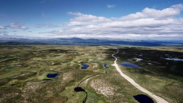Flying sideways, Flatruetv&auml;gen dirt road cutting through tundra landscape of Flatruet high fell Plateau with ponds and heather, with V&aring;l&aring;dalen Nature Reserve mountains on the horizon, J&auml;mtland Sweden