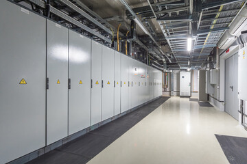 The interior of an electrical equipment room features neatly arranged cabinets, warning signs, and...