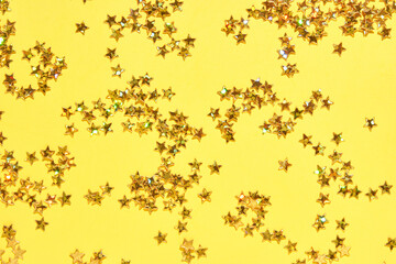 Sparkling golden star confetti on vibrant yellow background for festive celebrations and creative projects.