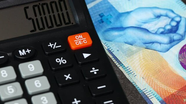 Swiss francs and calculator. Counting money and putting it on the desk next to the calculator with calculation. Switzerland money. Financial concept
