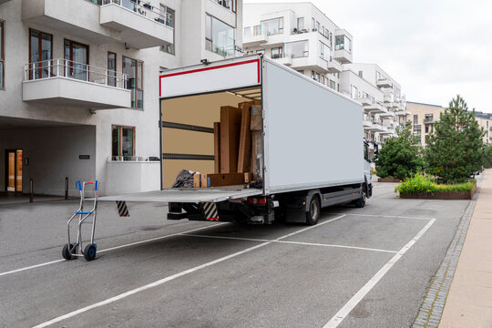 White delivery truck with tailgate open in front of modern residential buildings. Copy space.