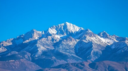 Fototapeta premium Snow-capped mountain peaks rise majestically against a vibrant blue sky, showcasing the serene beauty of a winter landscape in a pristine natural setting.