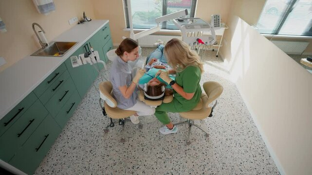 Blonde Woman Dentist with Assistant Treat Teeth of Female Patient with Special Instrument. Treatment of Caries and Plaque in Dental Clinic. Concept of Medicine and Healthcare. Slow Motion.