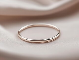 Thin silver bracelet with subtle hammered texture, resting on light grey fabric, minimalist jewelry concept