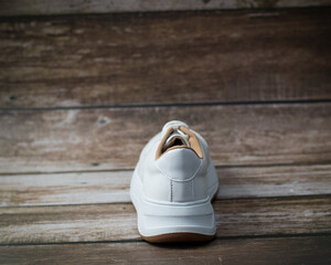 Elegant white eco-leather sneakers with brown sole detail, back view., on a wooden background