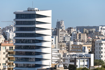 Modern office building towering over smaller residential buildings in a city center of Nicosia. Cyprus