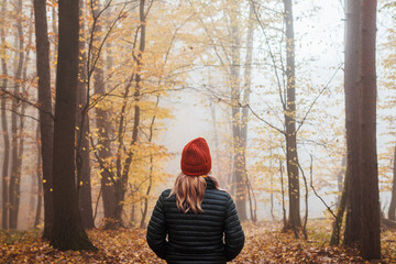 Woman with jacket and knitted hat enjoying walk in autumn forest in fog. Digital detox and harmony...