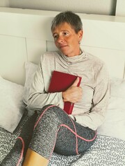 Portrait of a young adult woman, thoughtful, sitting in bed, with a book in her hand. Thoughtful...