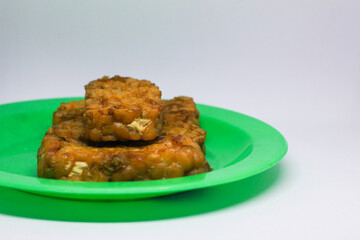 Fried tempeh food is served on a small green plate with a white background