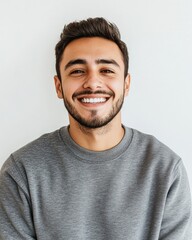 Fototapeta premium Happy Latin man smiling warmly in a cozy gray sweatshirt against a plain background