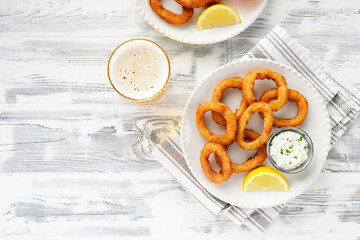 Delicious crispy fried calamari rings with white sauce and glass of beer. white wooden background, top view