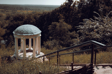 This peaceful gazebo overlooks a stunning landscape of rolling fields and forest. The soft sunlight...