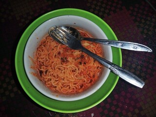 A noodle dish with savory spicy red sauce served in white and green bowls on a dark background.