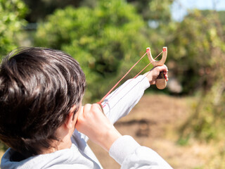 Boy aiming a slingshot in a sunny outdoor environment