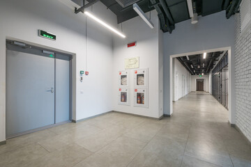 A long office corridor with a green emergency exit sign above a gray door. Loft-style .decor.