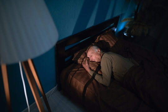 Above top view elderly mature man sleeping on soft pillow under blanket, dreams at night. Aged grandfather lying on side in comfortable bed.