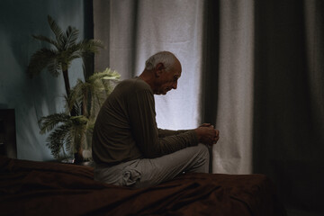 Silhouette depressed senior man 70s sits thoughtful looking down, melancholic male at night on the...