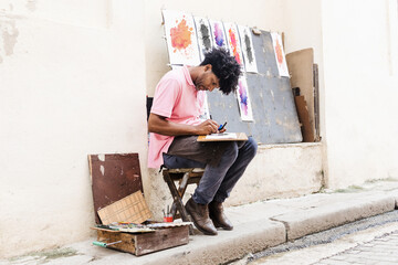 african american man artist or painter in the street painting on footpath in Latin America, Afro...