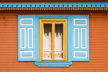 Wooden rustic window in small cottage house. Vintage yellow paint wall. Transparent glass window with lace curtain. Blue color shutter. Decorative triangle shapes pattern.