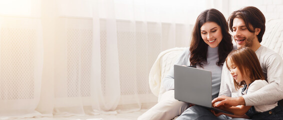 Happy family with little daughter using laptop together at home, watching movies or photos while sitting on floor in living room.