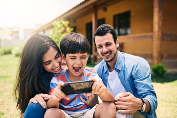 Excitement, love and phone with family in garden of new home together for gaming or streaming. Energy, smile or video with mother, father and happy son outdoor at apartment in summer for bonding