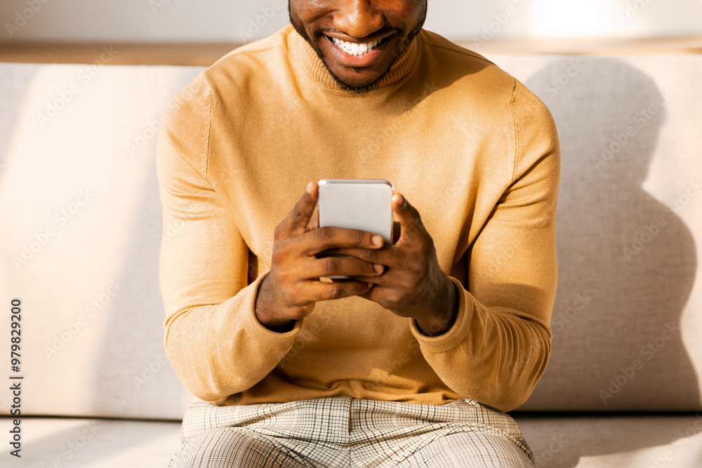 Poster mobile application. happy black man using smatphone playing games or texting sitting on sofa at home