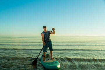 Man in shorts and sunglasses on a paddleboard with a paddle in the sea against the background