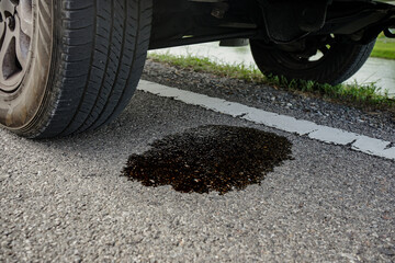 Black engine oil stains dripped under a broken down car parked on the road. Concept of car repair...
