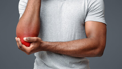 Young black man having pain in his elbow, touching his injured hand, close up