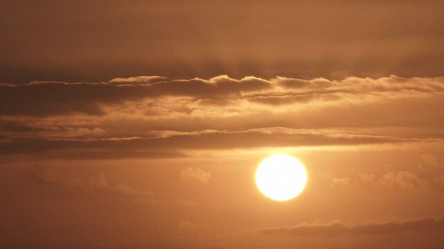 Fast and falling sun sets behind layers of clouds on a warm summer sky, time lapse.