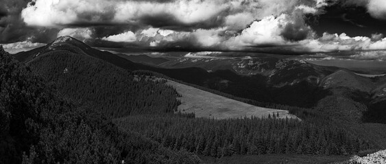 The dense forests on the hills lead up to a higher mountain ridge, all under a sky filled with...