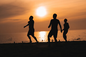 Silhouettes of Asian men playing beach soccer on a beach by the sea at sunset