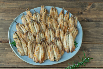 A plate of fried anchovies with a blue plate and a wooden table.