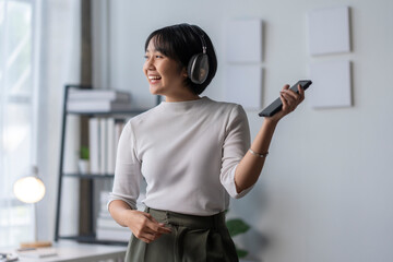 Young woman is enjoying music through headphones and holding smartphone in her hand