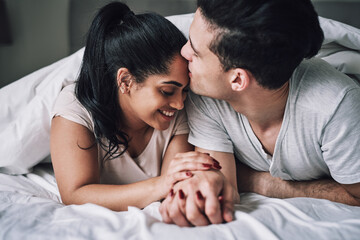 Kiss, happy and couple in bedroom for love, romance and embrace to wake up together on weekend. Apartment, house and woman with man holding hands for relationship, bonding and commitment in bed