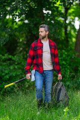 Bearded lumberjack. Lumberjack brutal bearded man in checkered shirt and ax in forest. Serious lumberjack holding axe and looking away outdoors. Lumberjack worker.
