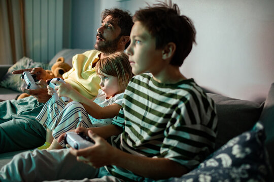 Father playing video games with his son and daughter at night in the living room