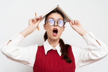 surprised young woman holding open book above her head, wearing glasses, with raised eyebrows and...