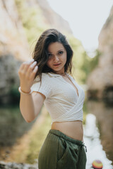 A woman in a white top and green pants stands confidently outdoors, showcasing a serene and...